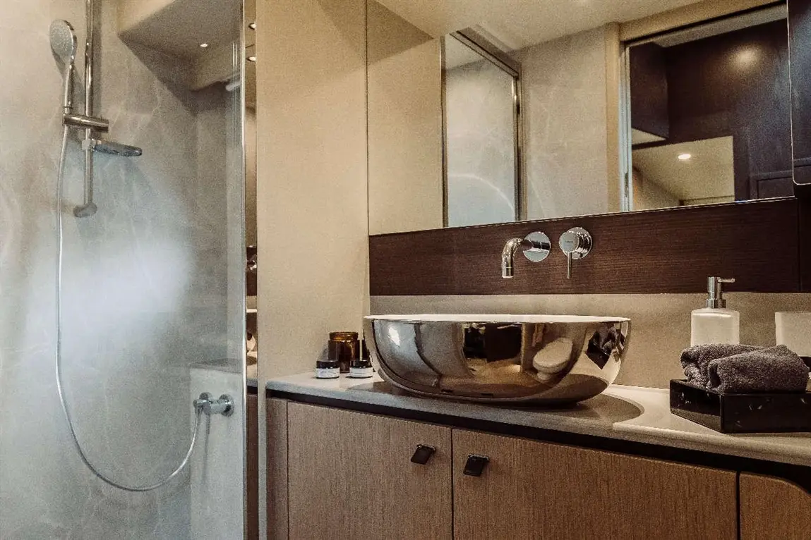 Modern bathroom featuring a walk-in shower, stylish round sink, and wooden cabinetry with towels and toiletries.